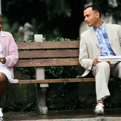 Forest Gump siedzi na ławce z walizką, obok niego siedzi kobieta.
