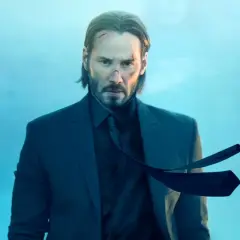 John Wick 5: Keanu Reeves w garniturze, z bliznami na twarzy, wpatruje się w obiektyw na tle błękitnego, mglistego nieba.