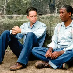 Skazani na Shawshank obsada: Tim Robbins i Morgan Freeman siedzą przy kamiennym murze, w więziennych strojach.