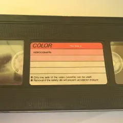 Czarna kaseta wideo z etykietą "COLOR videocassette". Widać dwie rolki taśmy.