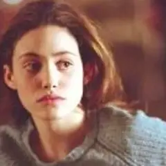 Emmy Rossum w szarym swetrze, aktorka znana z filmów, seriali i programów, zamyślona.