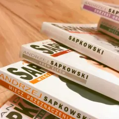 Stos książek Andrzeja Sapkowskiego, idealny przewodnik, jak czytać Wiedźmina. Widoczne tytuły: "Chrzest Ognia", "Wieża Jaskółki", "Czas Pogardy", "Krew Elfów", "Miecz Przeznaczenia".