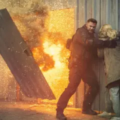 Mężczyzna w kamizelce taktycznej chroni kobietę przed eksplozją, jak w najlepszych filmach akcji.