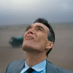 Oppenheimer patrzy w niebo, w tle mglisty krajobraz z pojazdami.