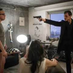 Mężczyzna w czarnym płaszczu celuje z pistoletu w drugiego mężczyznę. Scena przypomina moment, gdy można poczuć się jakby się "ślepnac od świateł 2".