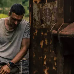 Zmęczony mężczyzna opiera się o zardzewiały metal. Prosta sprawa, obsada w trudnej sytuacji.