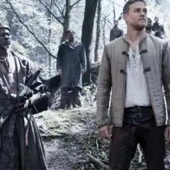 Król Artur i jego towarzysze w lesie, przygotowujący się do walki. W tle widać innych wojowników, a na pierwszym planie dwóch mężczyzn z mieczami, gotowych do akcji. Król Artur legenda miecza.