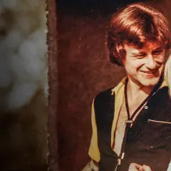 Uśmiechnięty mężczyzna w stylu lat 70. rozmawia z kobietą. Scena jak z filmu "Tulipan".