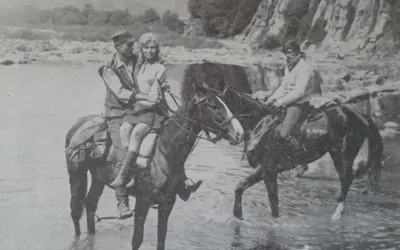 Para z "Wilczych ech" na koniach w rzece. W tle skaliste zbocze i drzewa.