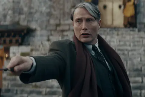 Mads Mikkelsen w roli Grindelwalda, z różdżką w dłoni, w filmie z serii "Fantastyczne zwierzęta".
