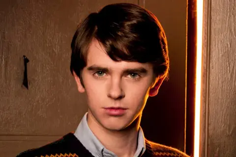 Freddie Highmore w swetrze i koszuli, zamyślony. Jego filmy, seriale i programy często poruszają złożone tematy.