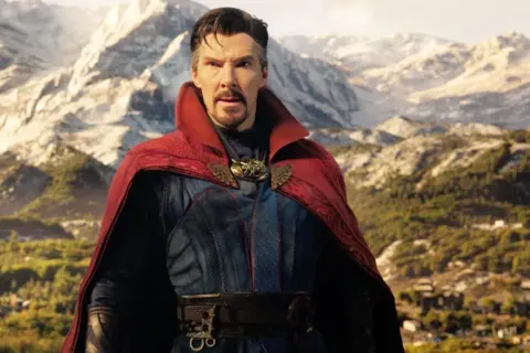 Doktor Strange w multiwersum obłędu obsada. Benedict Cumberbatch jako Strange w czerwonym płaszczu i niebieskim stroju na tle gór.
