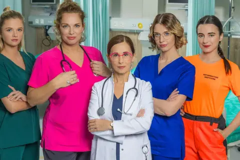 Pięć kobiet w strojach medycznych, obsada serialu "Szpital św. Anny", pozuje do zdjęcia w szpitalnym wnętrzu.