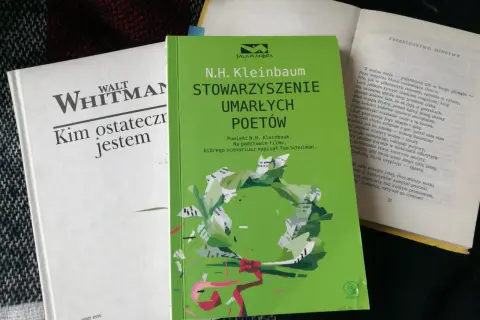 Zielona okładka książki "Stowarzyszenie Umarłych Poetów" N.H. Kleinbauma. Obok biała książka Walta Whitmana.