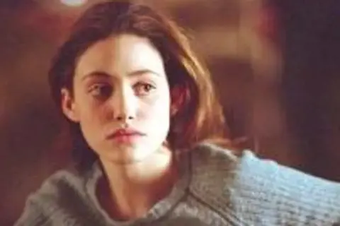 Emmy Rossum w szarym swetrze, aktorka znana z filmów, seriali i programów, zamyślona.