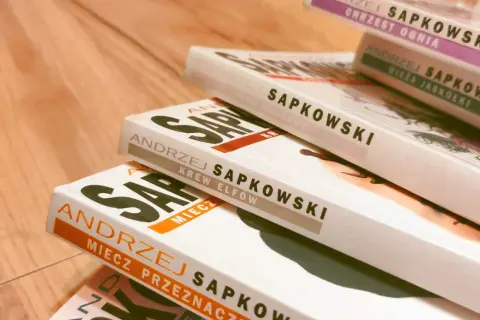 Stos książek Andrzeja Sapkowskiego, idealny przewodnik, jak czytać Wiedźmina. Widoczne tytuły: "Chrzest Ognia", "Wieża Jaskółki", "Czas Pogardy", "Krew Elfów", "Miecz Przeznaczenia".