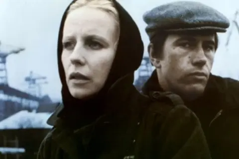 Kobieta w czarnym nakryciu głowy i mężczyzna w czapce, w tle stoczniowe dźwigi. Scena z filmu "Człowiek z żelaza".