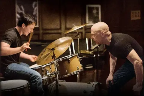 Whiplash obsada: młody perkusista ćwiczy pod okiem surowego nauczyciela. Intensywna lekcja w sali prób.