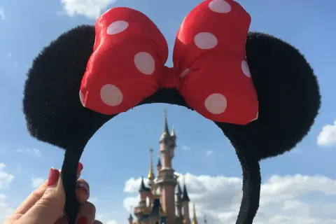 Opaska z uszami Myszki Miki i czerwoną kokardką w kropki, na tle zamku. Czyżby to początek przygody z księżniczki Disneya imiona?