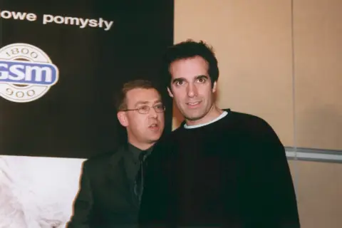 David Copperfield, w czarnym swetrze, stoi obok mężczyzny w garniturze.