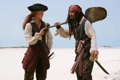 Elizabeth Swann i Kapitan Jack Sparrow, bohaterowie filmów "Piraci z Karaibów", stoją na piaszczystej plaży.