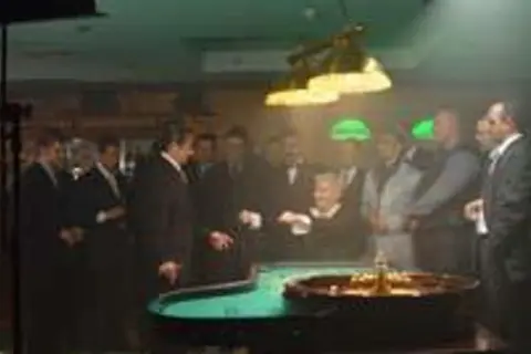 Wielki Szu obsada w kasynie, przy stole do ruletki. Mężczyźni w garniturach obserwują grę.