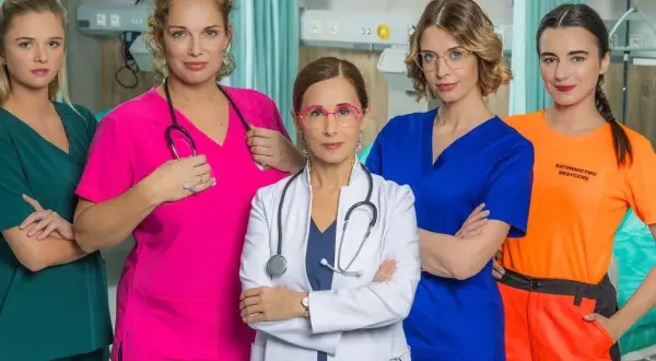 Pięć kobiet w strojach medycznych, obsada serialu "Szpital św. Anny", pozuje do zdjęcia w szpitalnym wnętrzu.