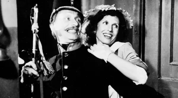 Uśmiechnięta para z filmu "C.K. Dezerterzy" - mężczyzna w mundurze i kobieta w kapeluszu.