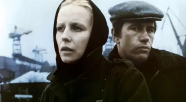 Kobieta w czarnym nakryciu głowy i mężczyzna w czapce, w tle stoczniowe dźwigi. Scena z filmu "Człowiek z żelaza".