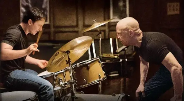 Whiplash obsada: młody perkusista ćwiczy pod okiem surowego nauczyciela. Intensywna lekcja w sali prób.