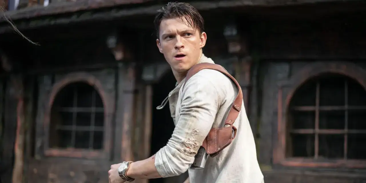 Tom Holland jako Nathan Drake w filmie Uncharted 2, w akcji, z pistoletem w kaburze na ramieniu, w otoczeniu starych budowli.