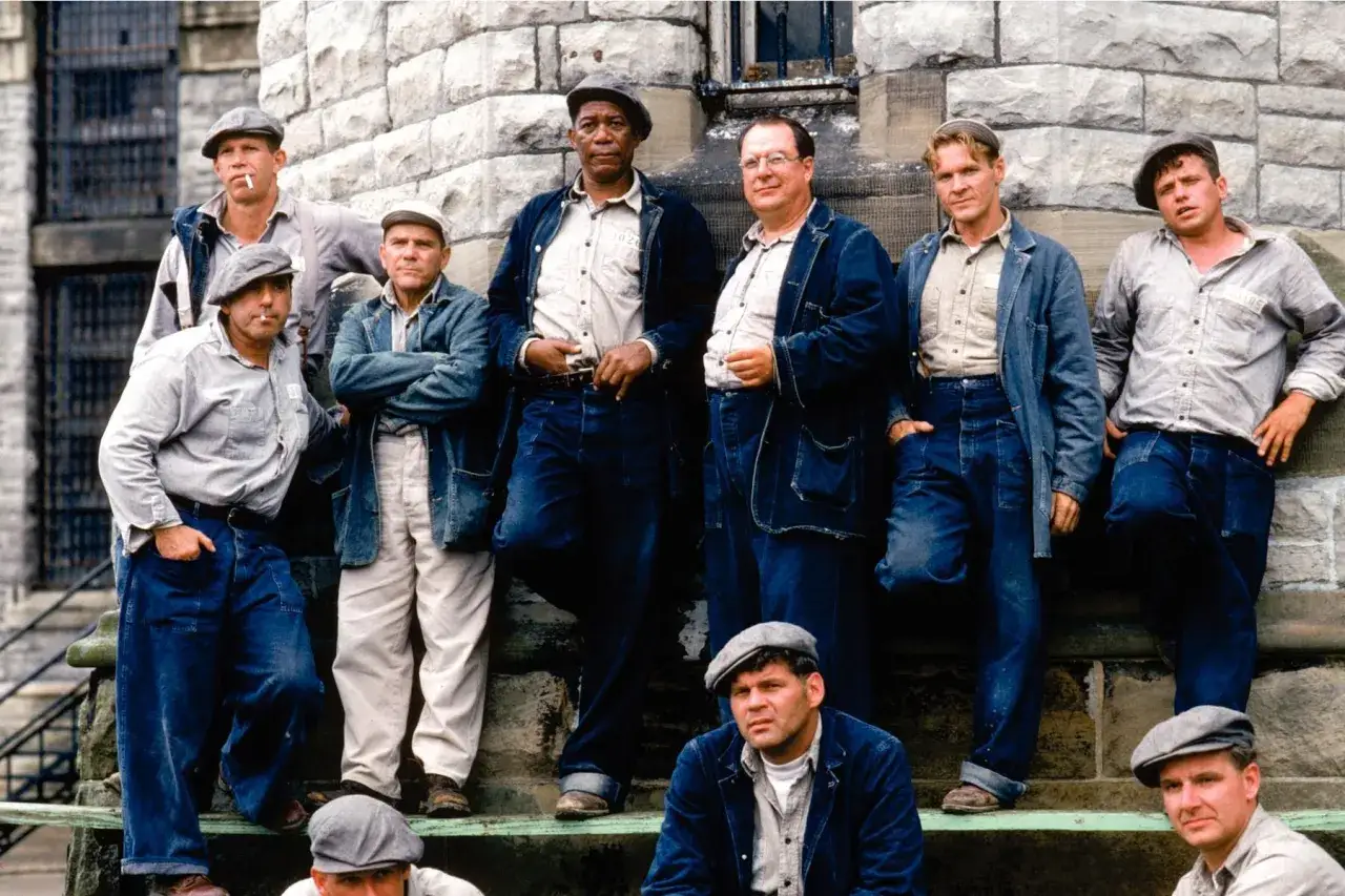 Skazani na Shawshank obsada: Morgan Freeman, Tim Robbins i inni więźniowie pozują na tle kamiennej ściany.