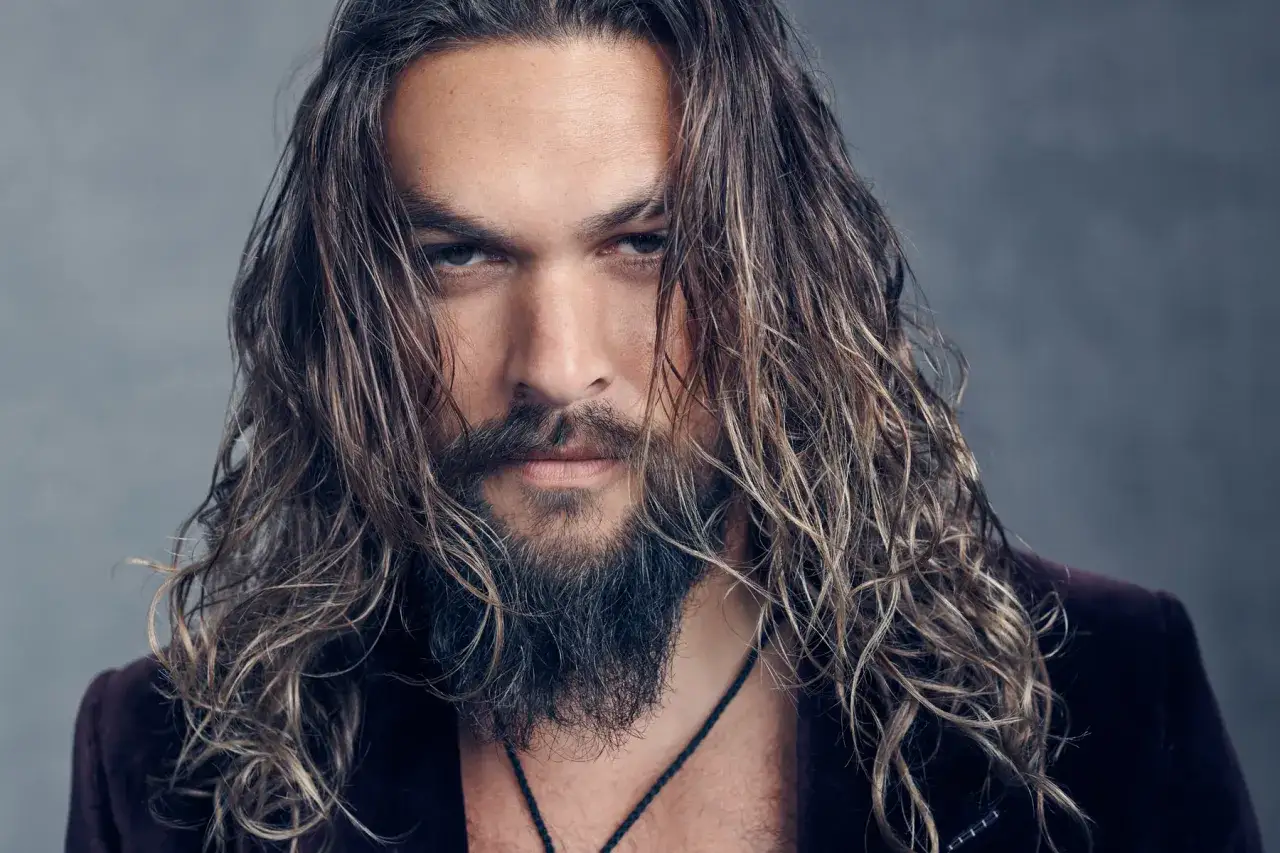 Jason Momoa, znany z filmów, seriali i programów, z burzą włosów i zarostem.