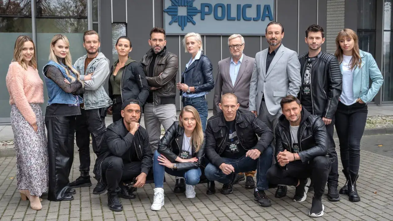 Cała gliniarze obsada pozuje przed budynkiem policji.