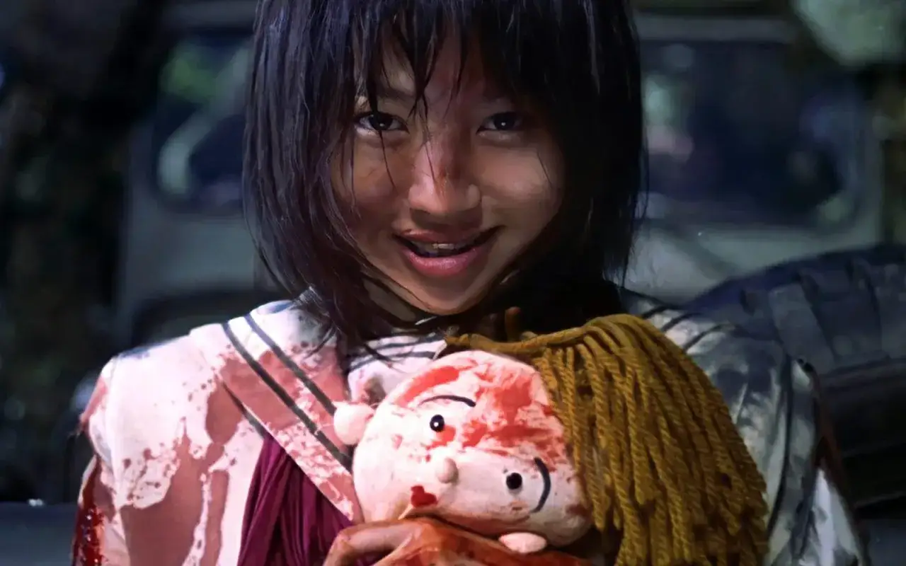 Uśmiechnięta dziewczyna w zakrwawionej szkole trzyma pluszową lalkę. To przerażający obraz z filmu battle royale.