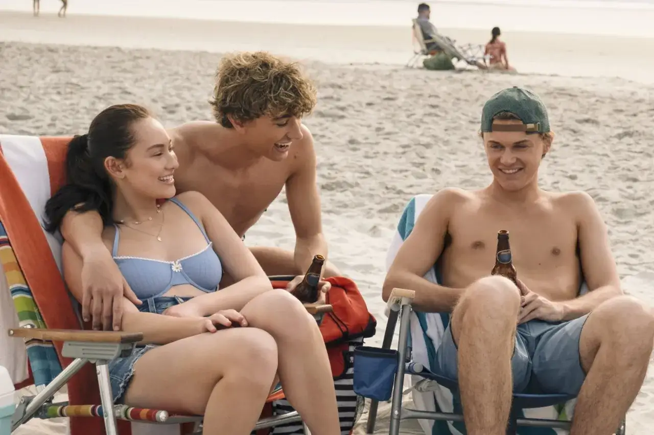 Trzech młodych ludzi cieszy się słońcem na plaży, pijąc napoje. To scena jak z filmu 