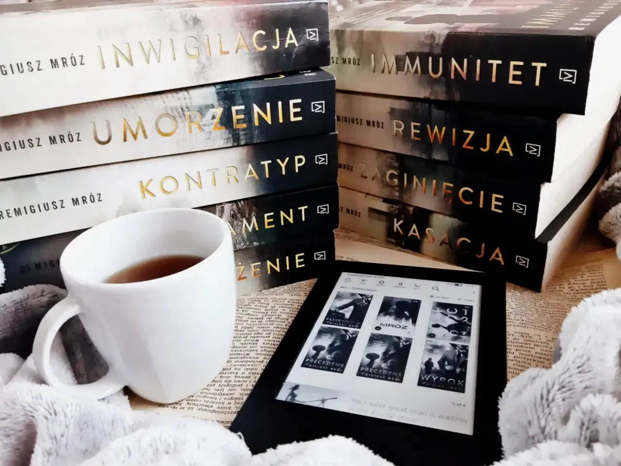 Książki Remigiusza Mróza w chyłkiej kolejności, kubek herbaty i czytnik Kindle. Idealny zestaw na relaksujący wieczór.