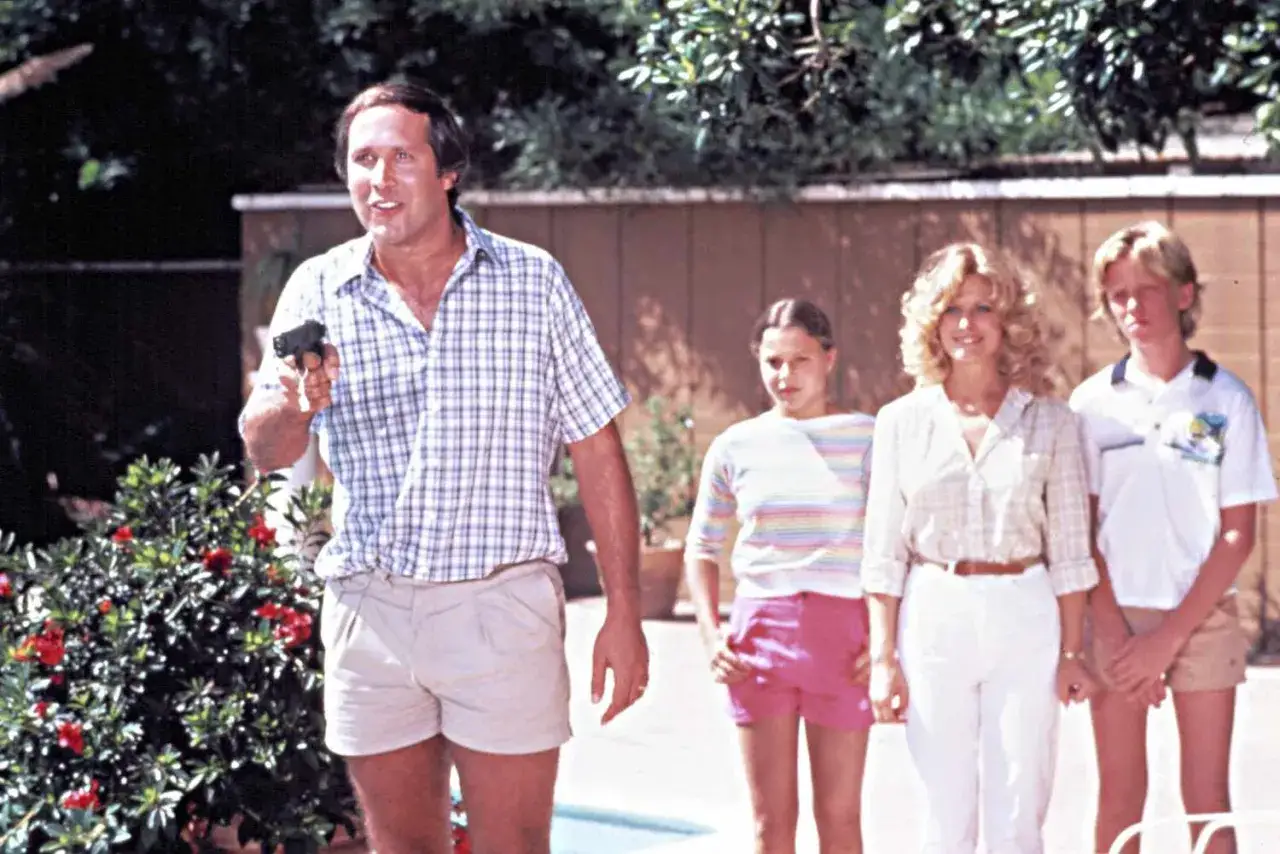 Clark Griswold z pistoletem, obok żony i dwójki dzieci. Rodzina Griswoldów w letnich strojach.