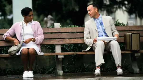 Forest Gump siedzi na ławce z walizką, obok niego siedzi kobieta.