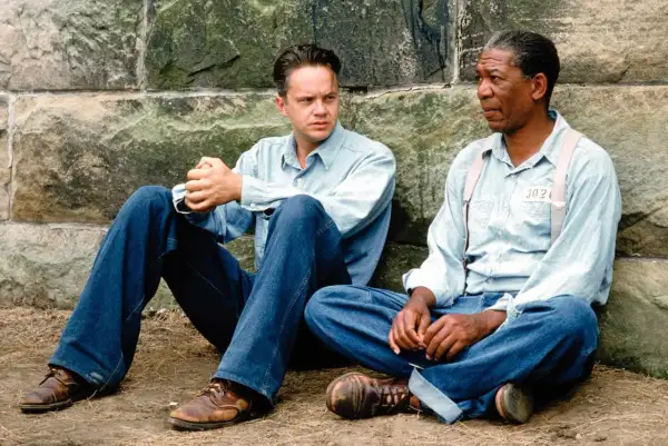 Skazani na Shawshank obsada: Tim Robbins i Morgan Freeman siedzą przy kamiennym murze, w więziennych strojach.