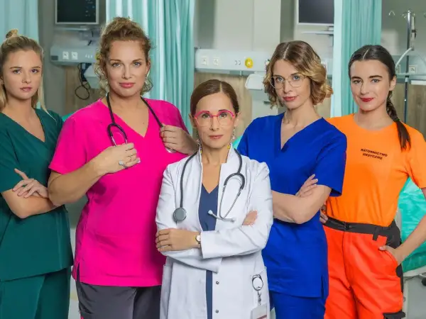 Pięć kobiet w strojach medycznych, obsada serialu "Szpital św. Anny", pozuje do zdjęcia w szpitalnym wnętrzu.