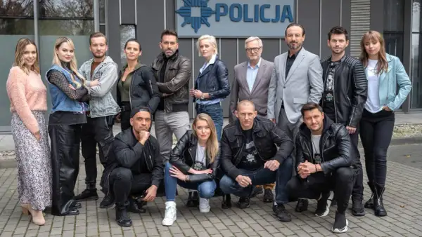 Cała gliniarze obsada pozuje przed budynkiem policji.