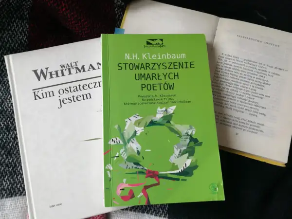 Zielona okładka książki "Stowarzyszenie Umarłych Poetów" N.H. Kleinbauma. Obok biała książka Walta Whitmana.