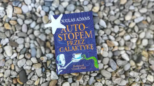 Okładka książki "Autostopem przez galaktykę" Douglasa Adamsa, z ilustracją Chrisa Riddella, leży na kamieniach.