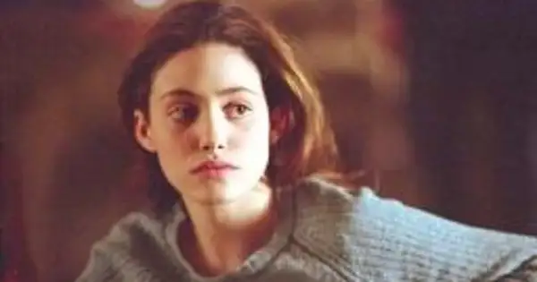Emmy Rossum w szarym swetrze, aktorka znana z filmów, seriali i programów, zamyślona.