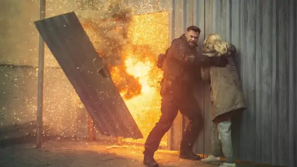 Mężczyzna w kamizelce taktycznej chroni kobietę przed eksplozją, jak w najlepszych filmach akcji.