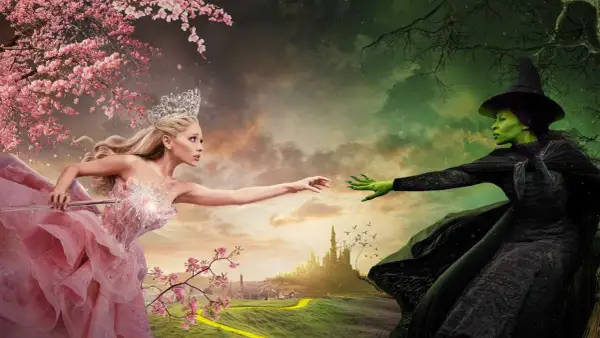 Królowa w różowej sukni i zielona wiedźma z "Wicked 2" wyciągają do siebie ręce na tle baśniowego krajobrazu.