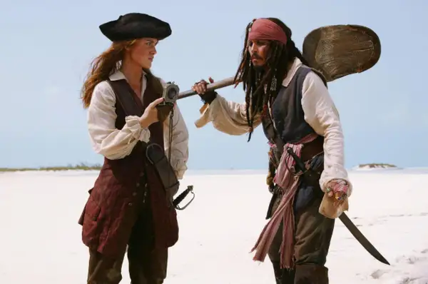 Elizabeth Swann i Kapitan Jack Sparrow, bohaterowie filmów "Piraci z Karaibów", stoją na piaszczystej plaży.