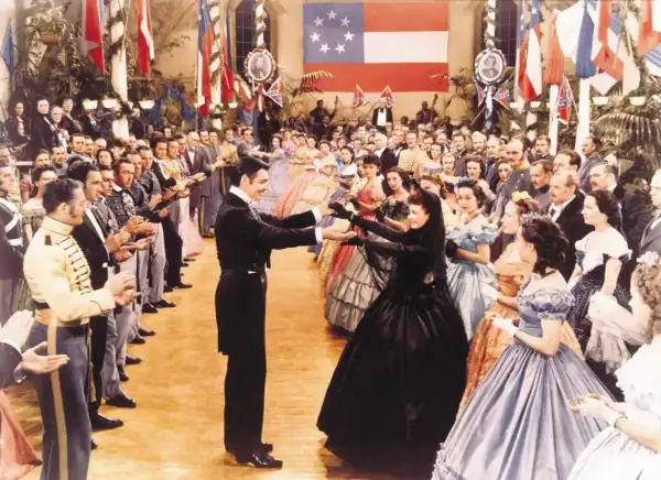 Scarlett O'Hara i Rhett Butler tańczą na balu. W tle widać całą obsadę filmu "Przeminęło z wiatrem" w historycznych strojach.