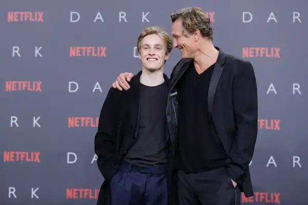 Uśmiechnięty młody aktor z serialu "Dark" i starszy kolega z obsady pozują na tle logo Netflix.